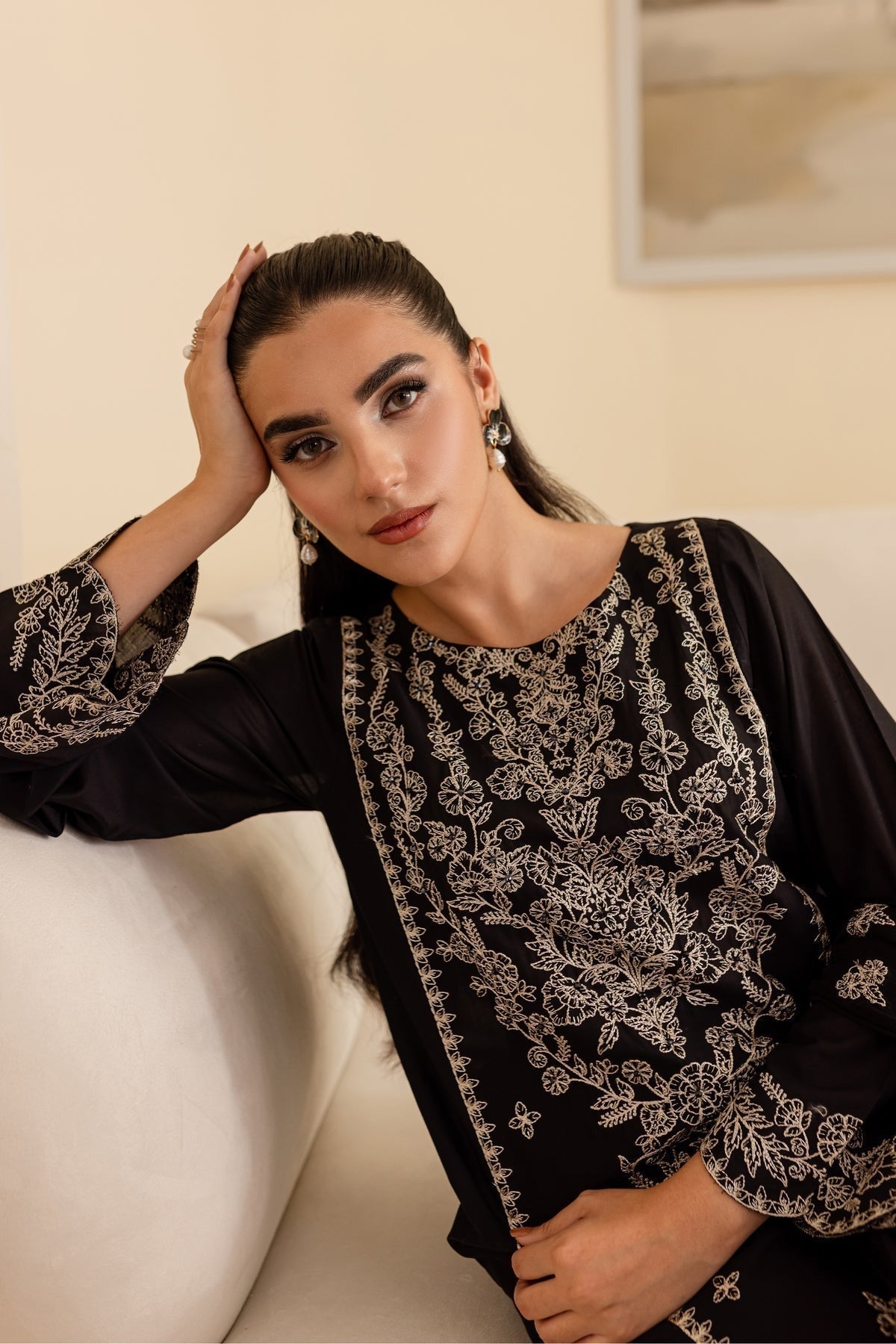 Woman wearing a black and white embroidered traditional outfit sitting on a white couch.